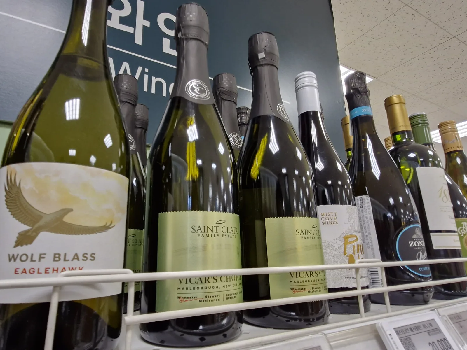 이마트 와인 매대 진열대에 세워진 생 클레어 비카스 초이스 소비뇽 블랑 버블 병들, 왼쪽에 울프 블라스 이글호크, 뒤편에 와인 Wine 안내판